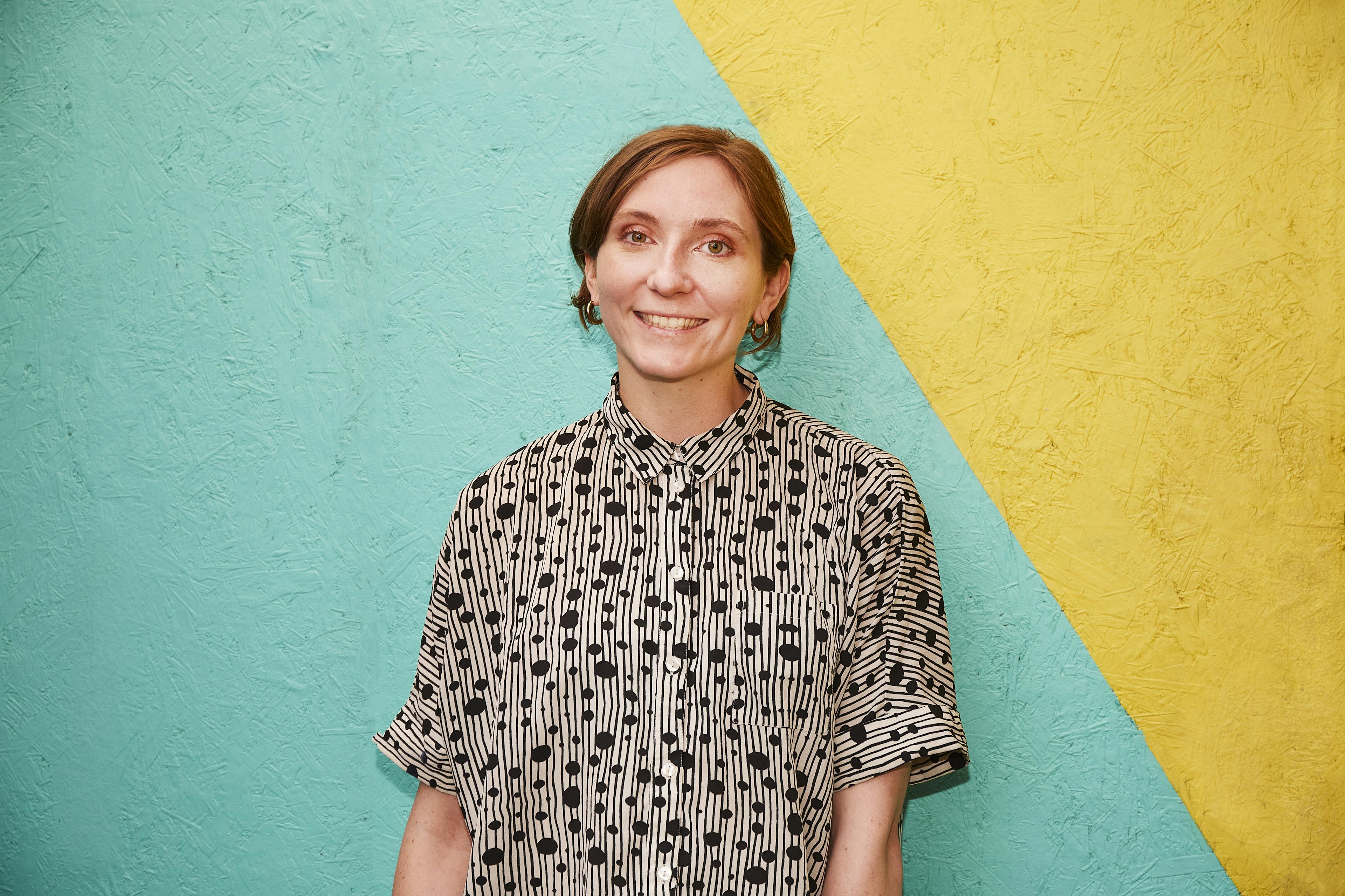 Rhio is smiling against a yellow and blue background.