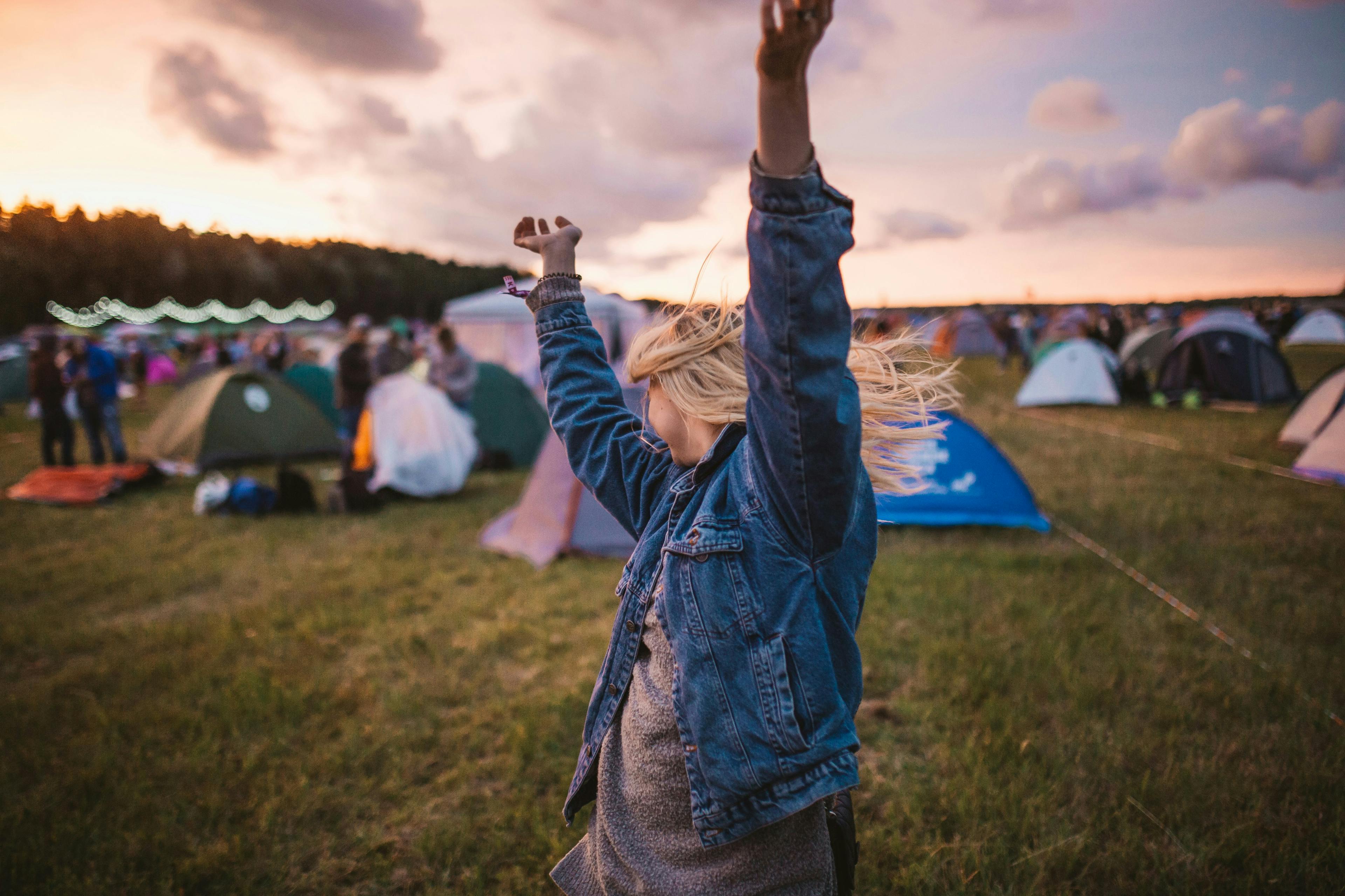 Girl in a field with tents – music festival – hands in the air