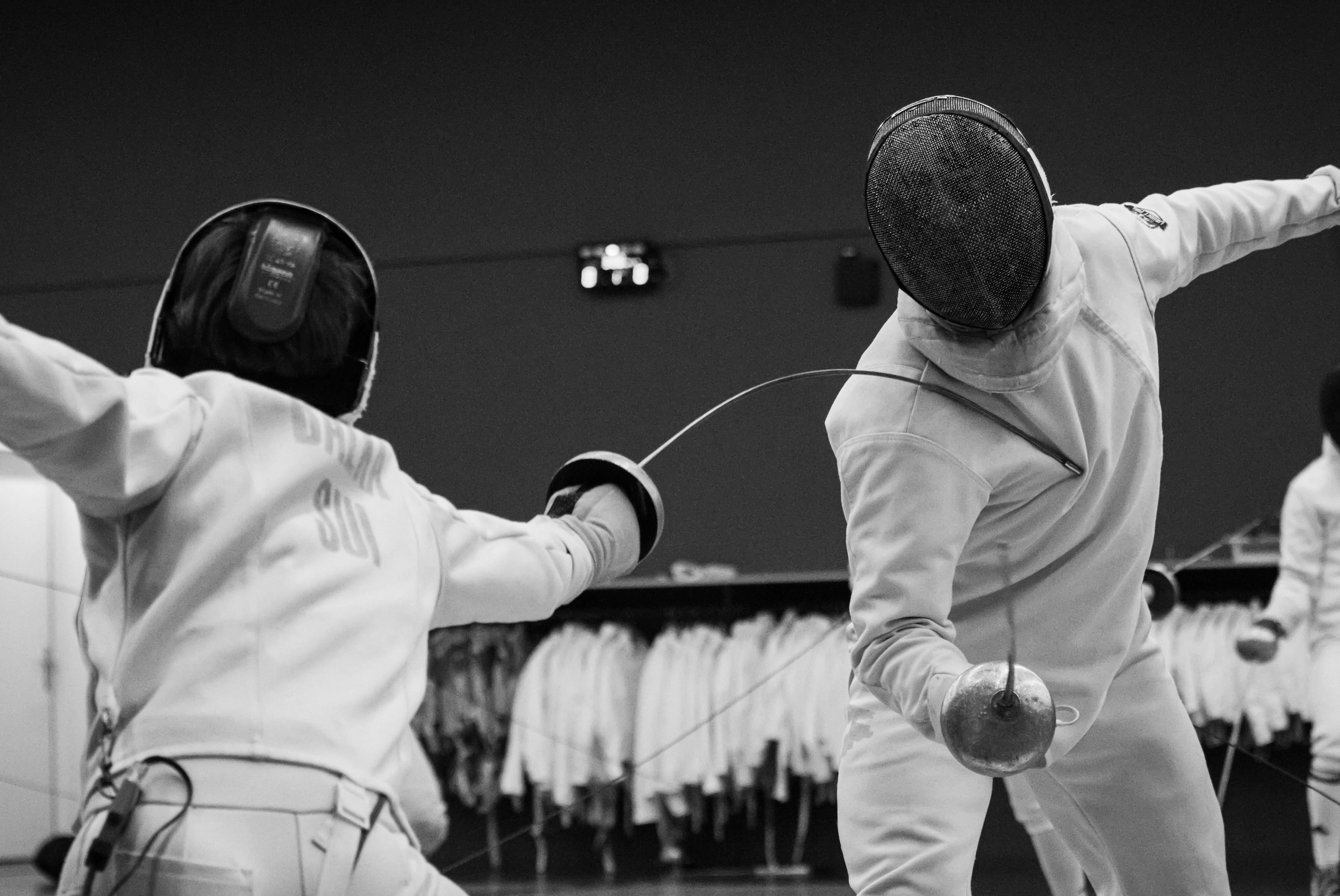 Two people fencing in full fencing uniforms - black and white photo