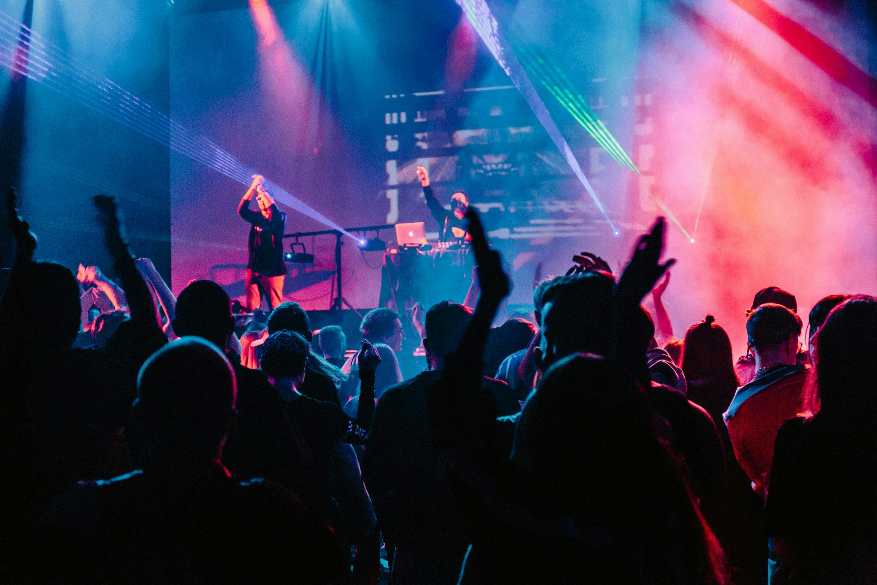 Concert scene – audience watching a performance with hands in the air against backdrop of blue and pink stage lighting
