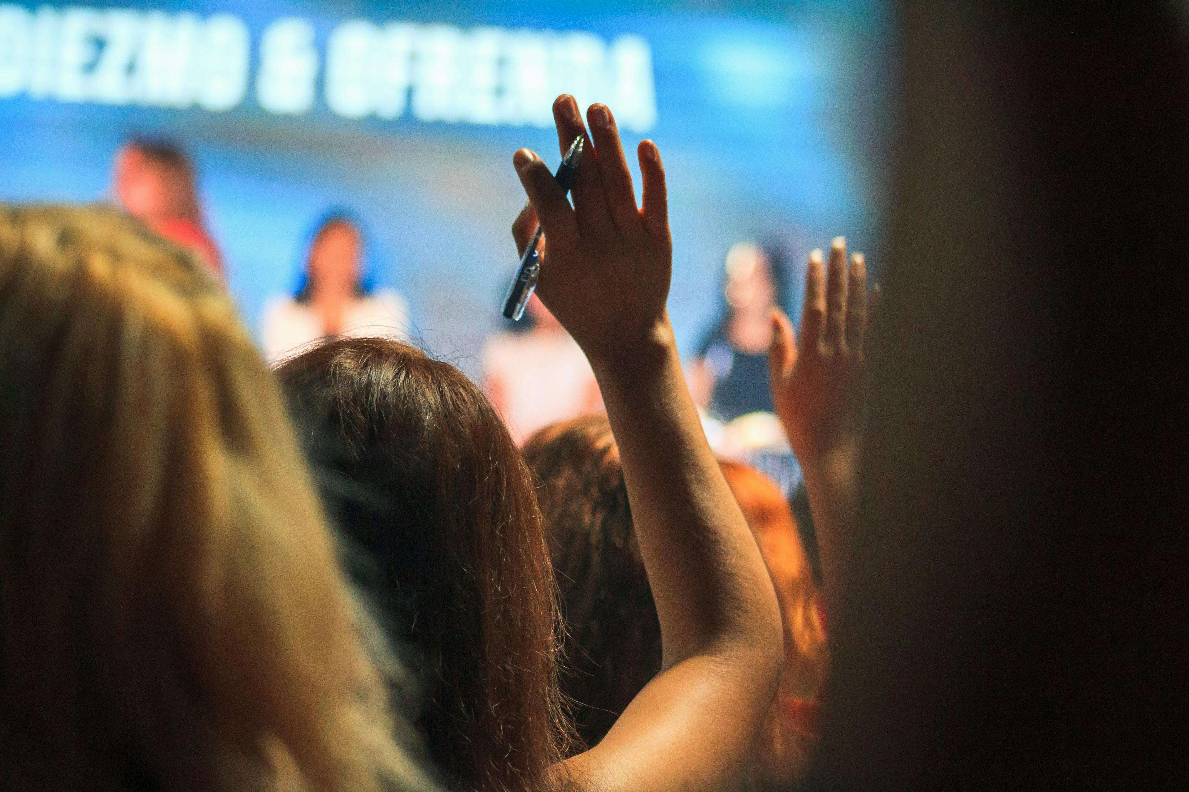 A close up of the back of people's heads in an audience for a conference event – some people with hands raised