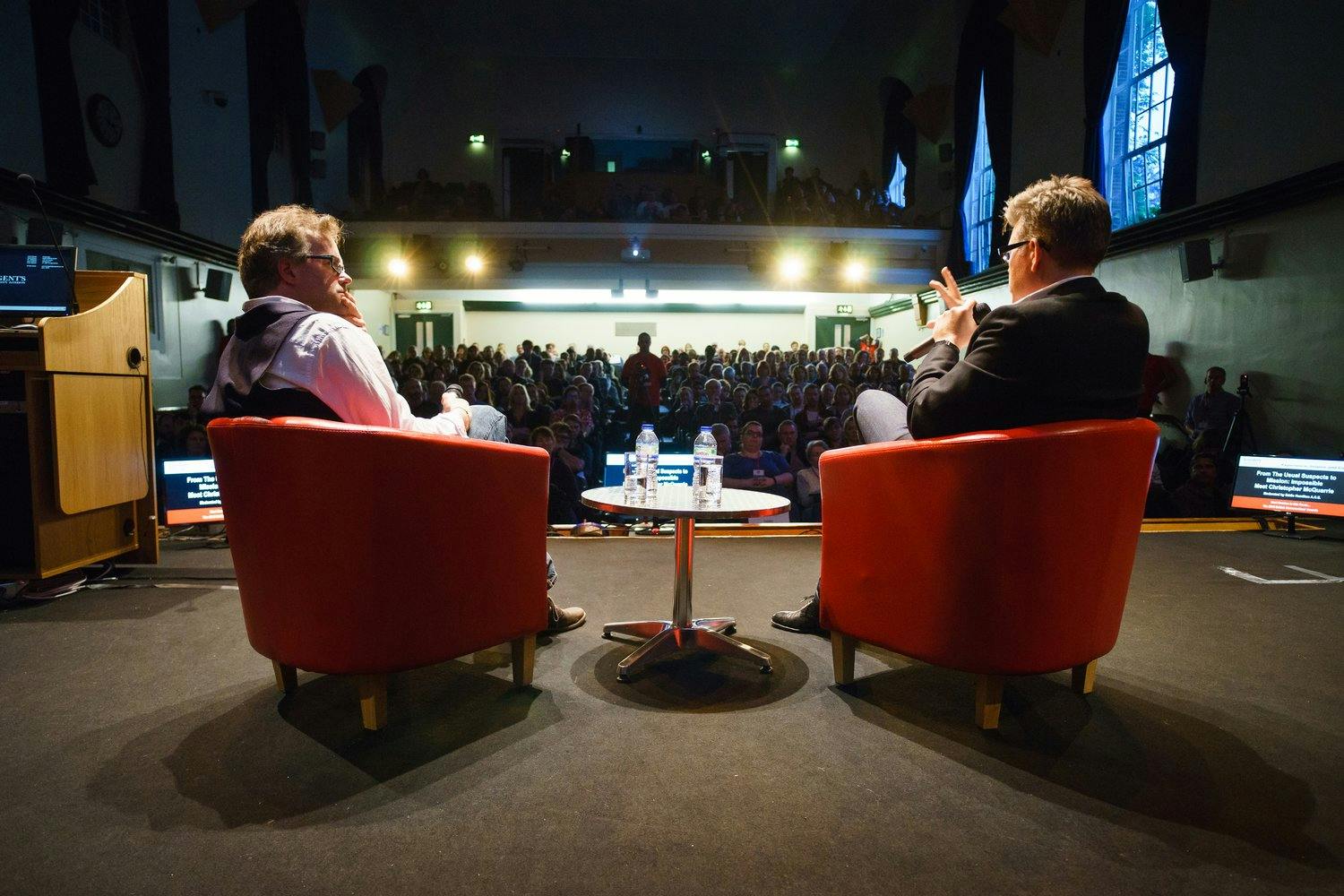 two men sitting in chairs in front of a large crowd