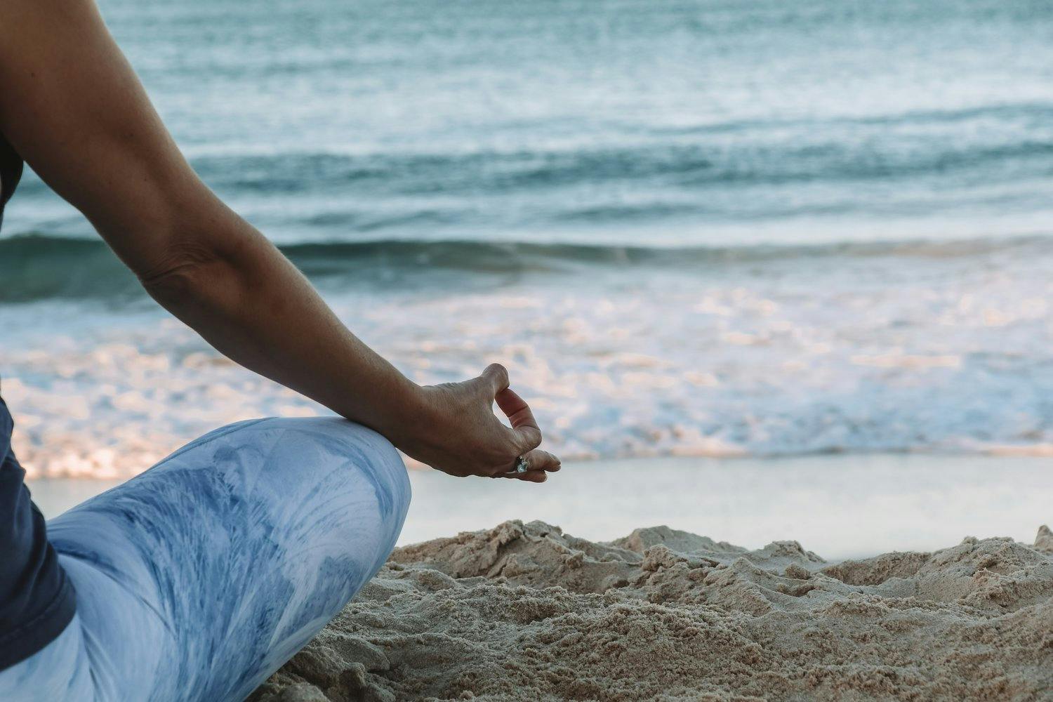 a person sitting in the sand with a hand in front of the ocean