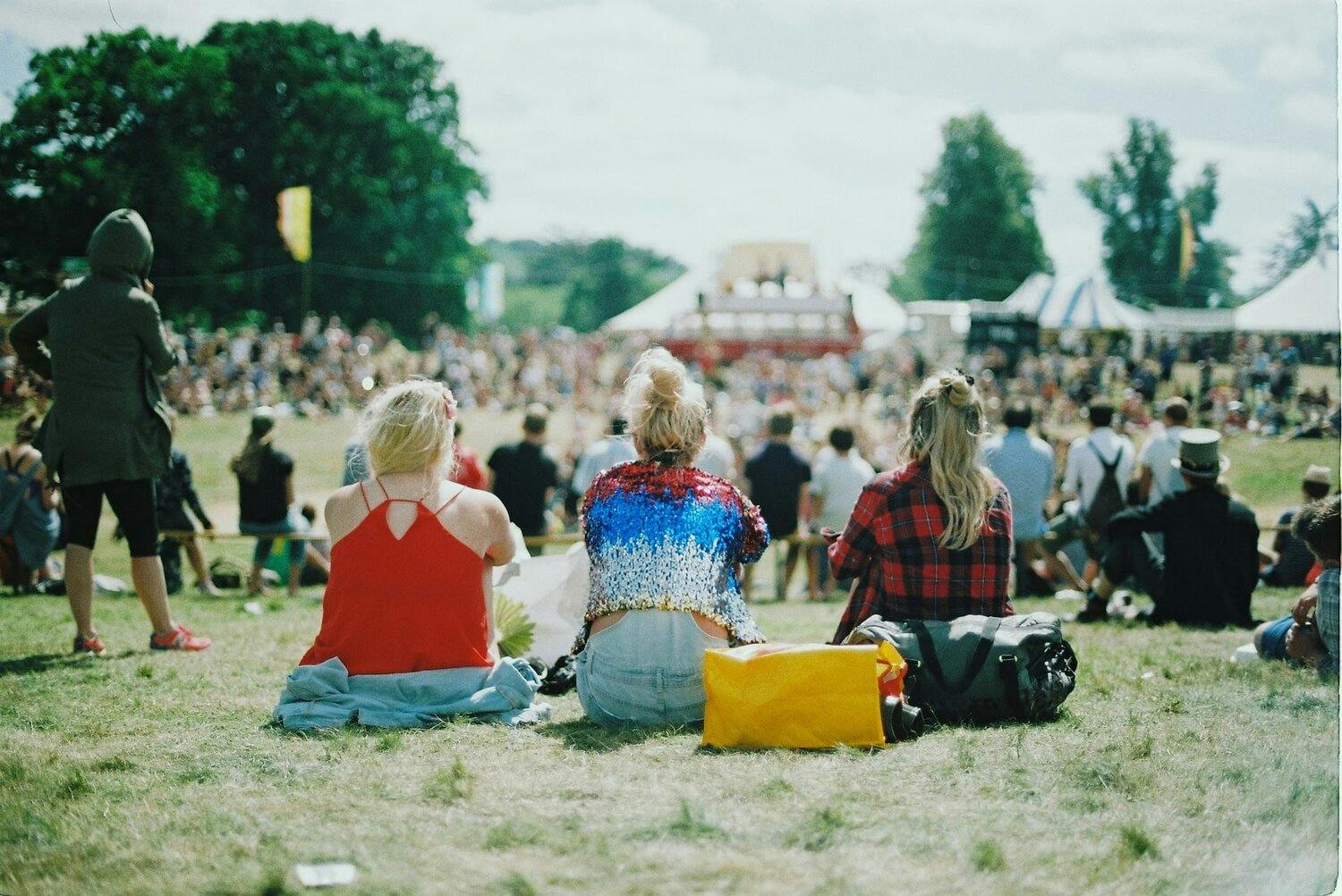 a group of women sitting on grass with a crowd in the background