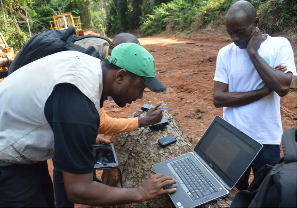 a group of men standing outside looking at a laptop