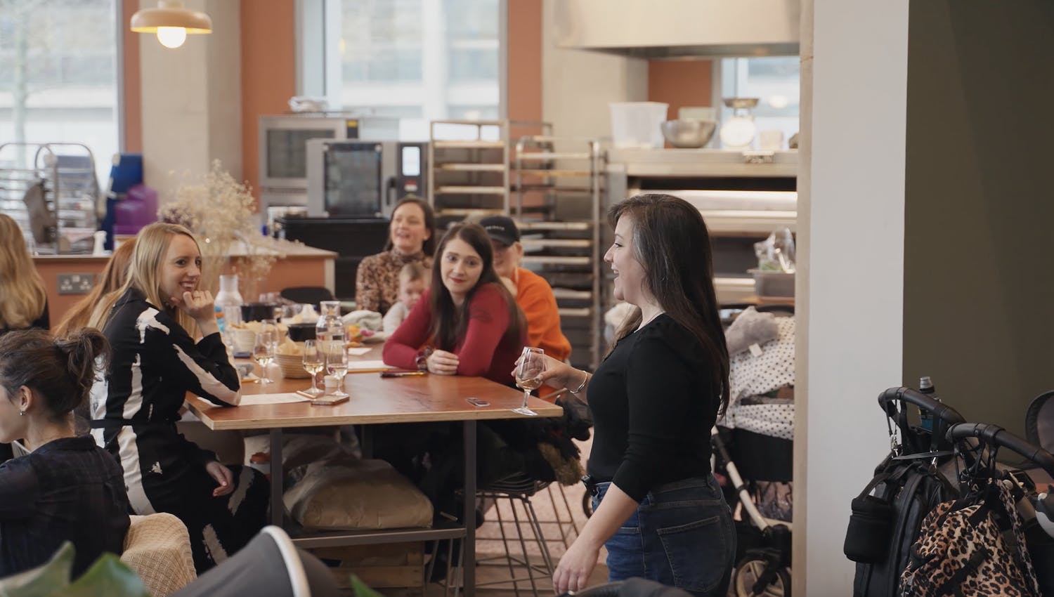 a group of people sitting at tables and drinking wine while one person is talking to them