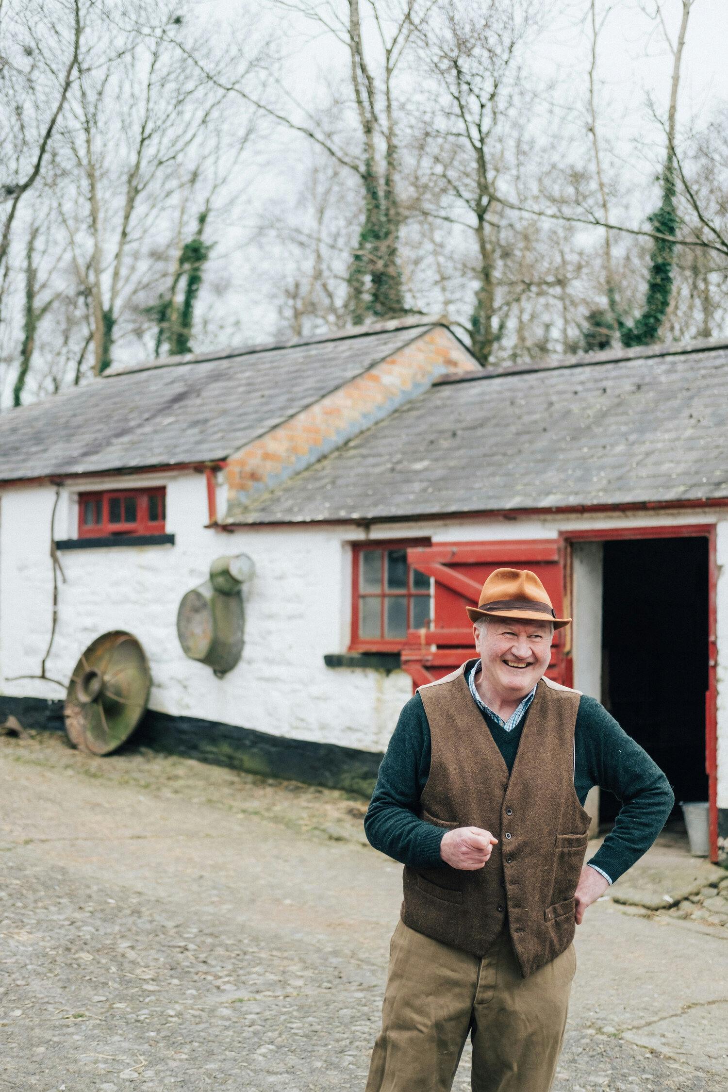a person in a brown vest and hat standing in front of a white building