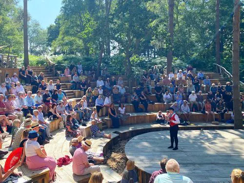 a group of people sitting on benches in a park and watching a performance