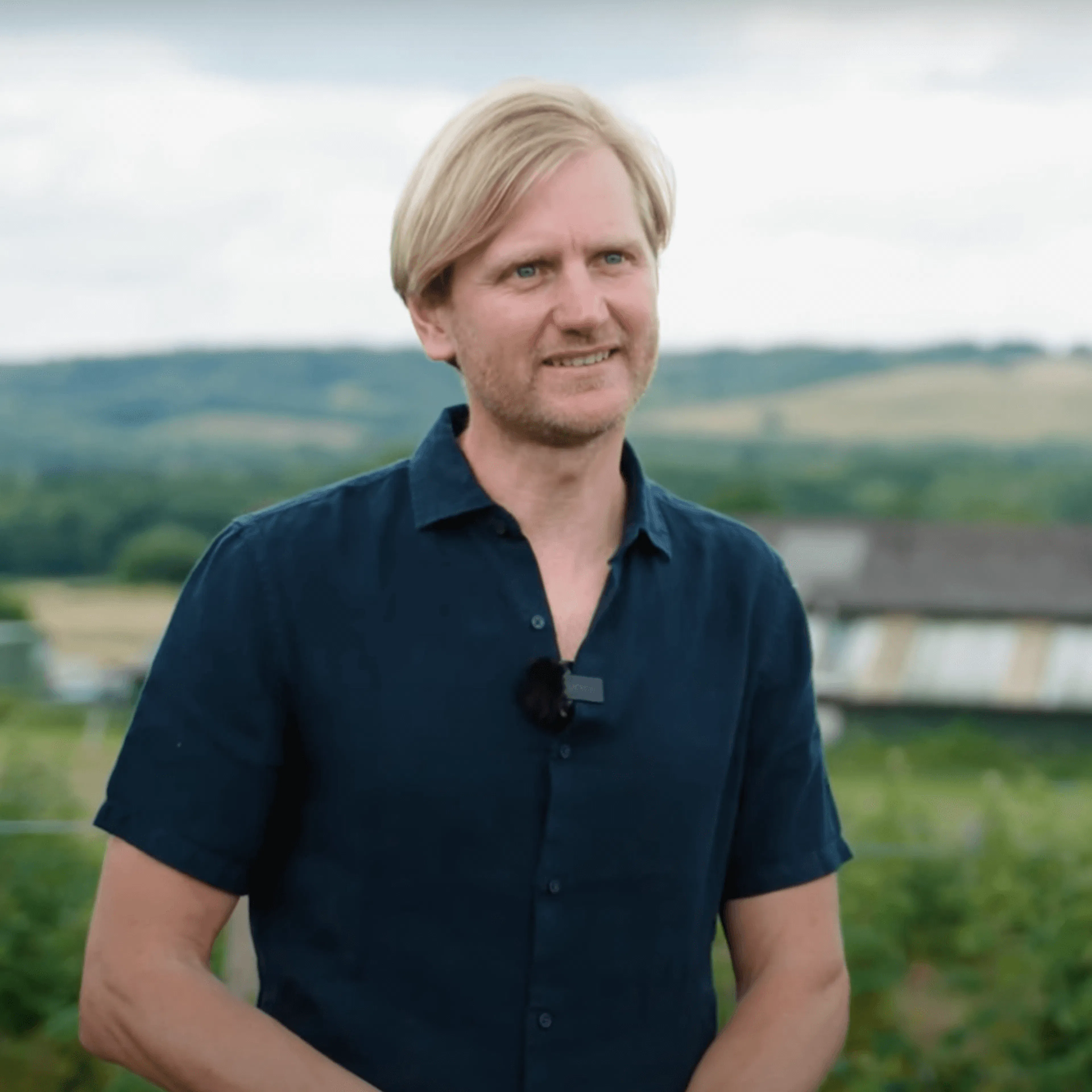 a man smiling with the farm in the background