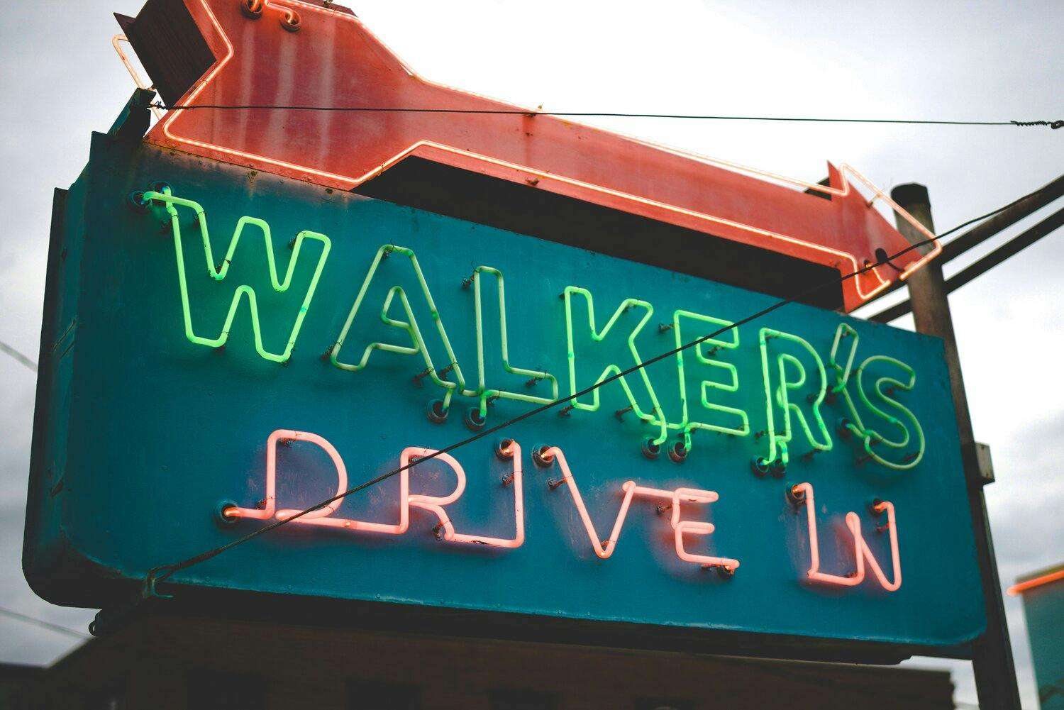 a neon sign on a building with an arrow and words walker's drive in