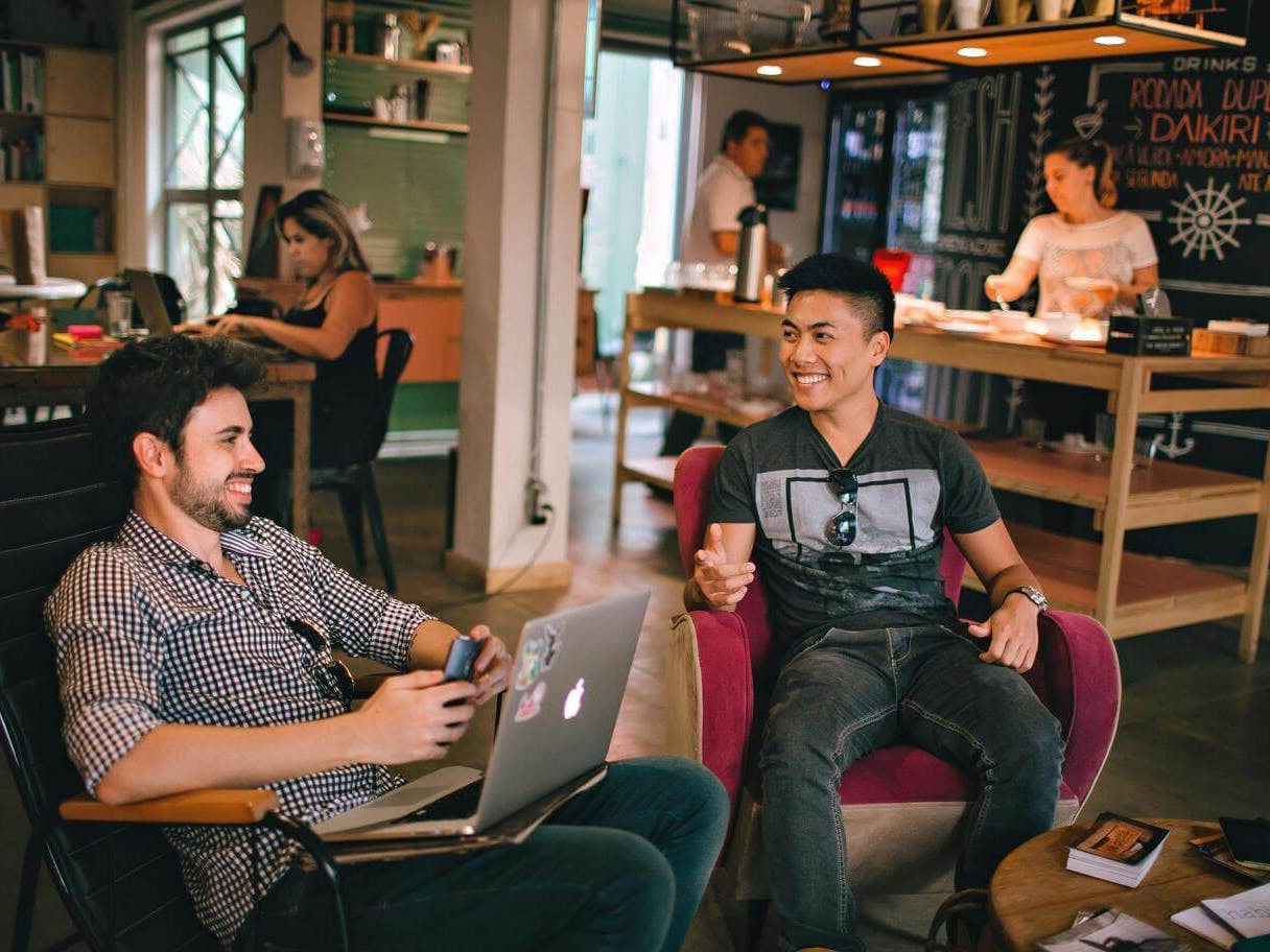 two men sat smiling with a laptop