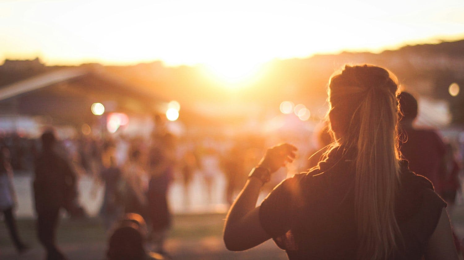 Blurry, sunny photo of a music festival with a girl to the forefront