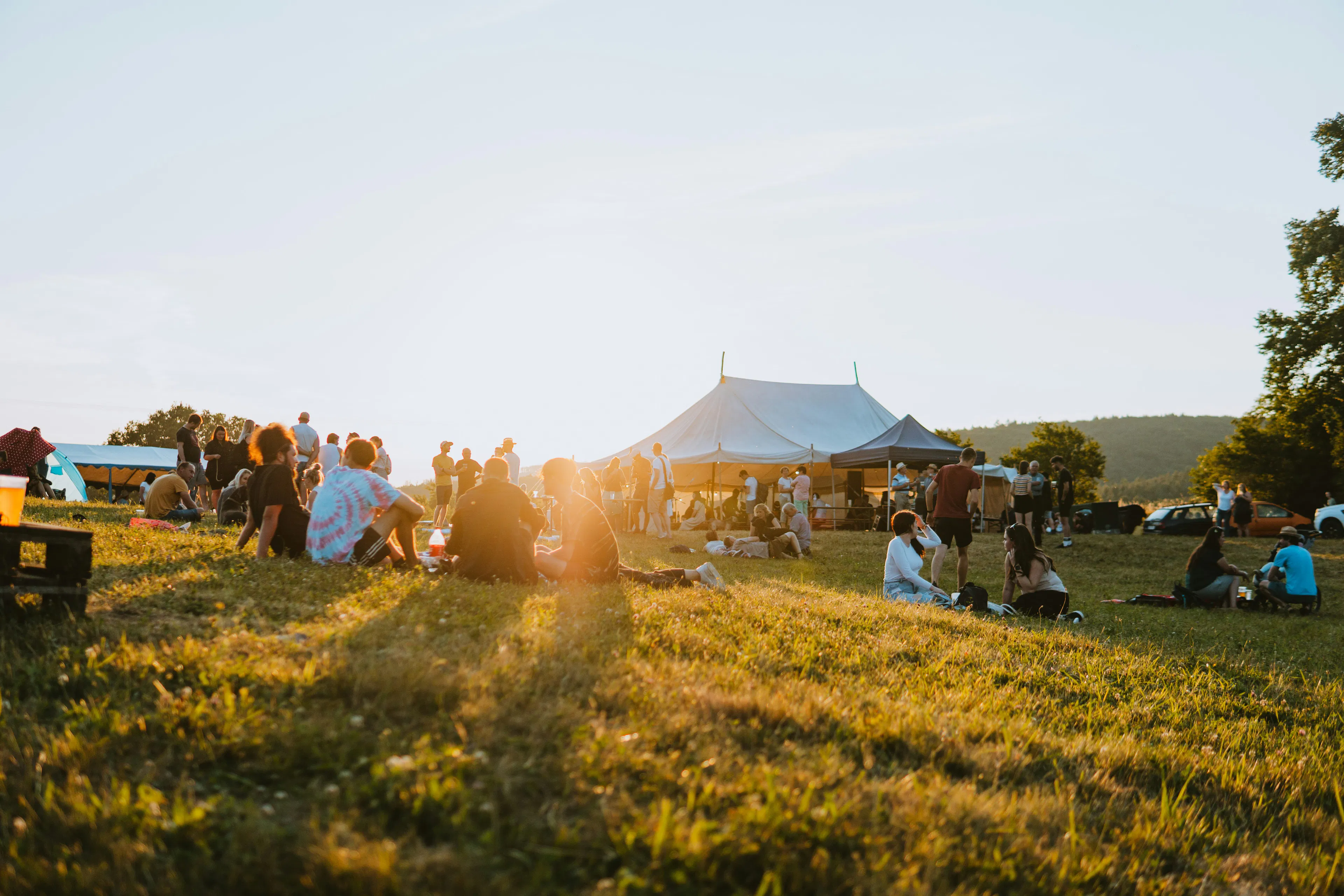 Field with people sitting on the floor at sunset and tents in the background