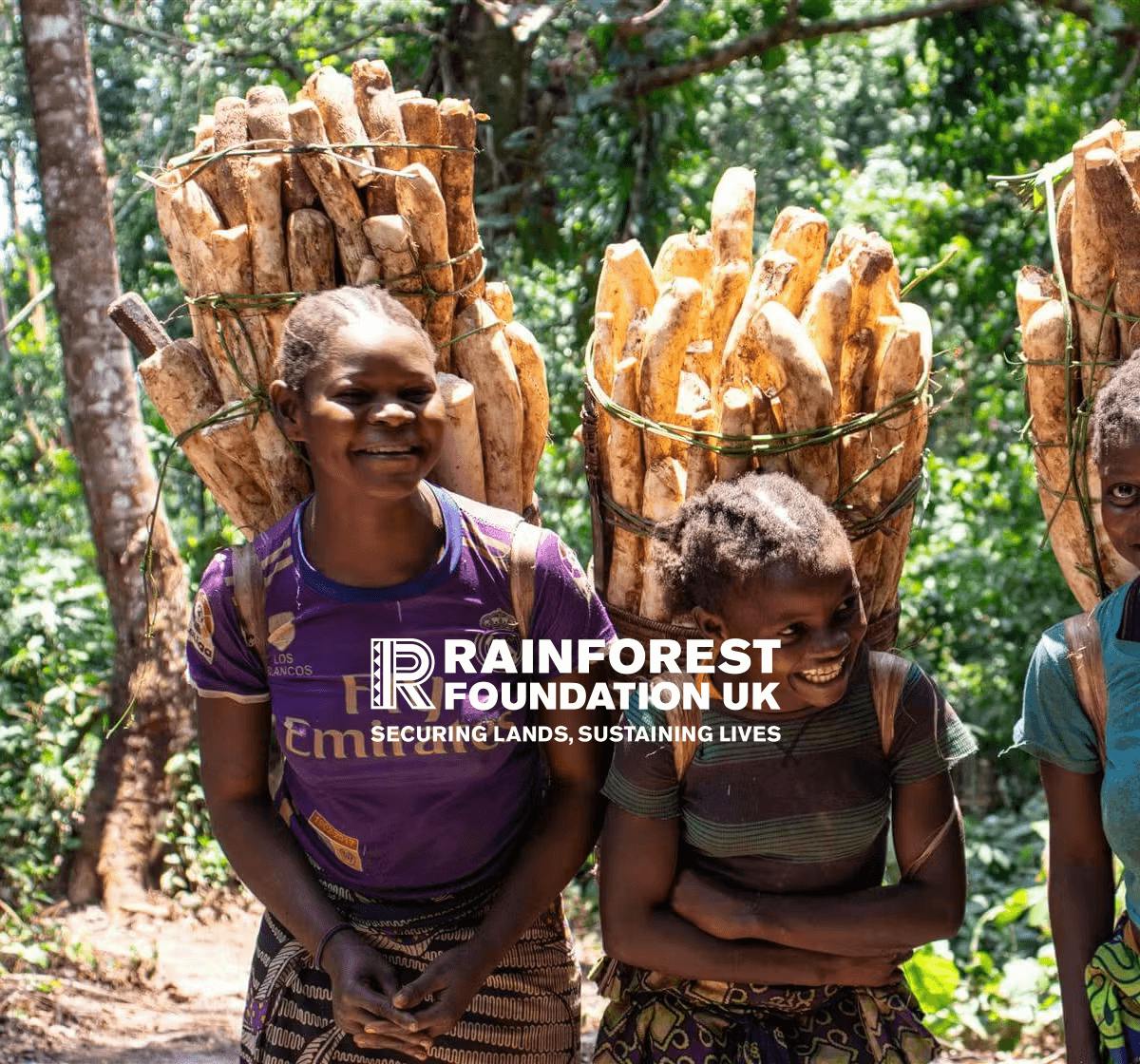 Two young women smiling in the rainforest with their harvest and the Rainforest Foundation UK logo