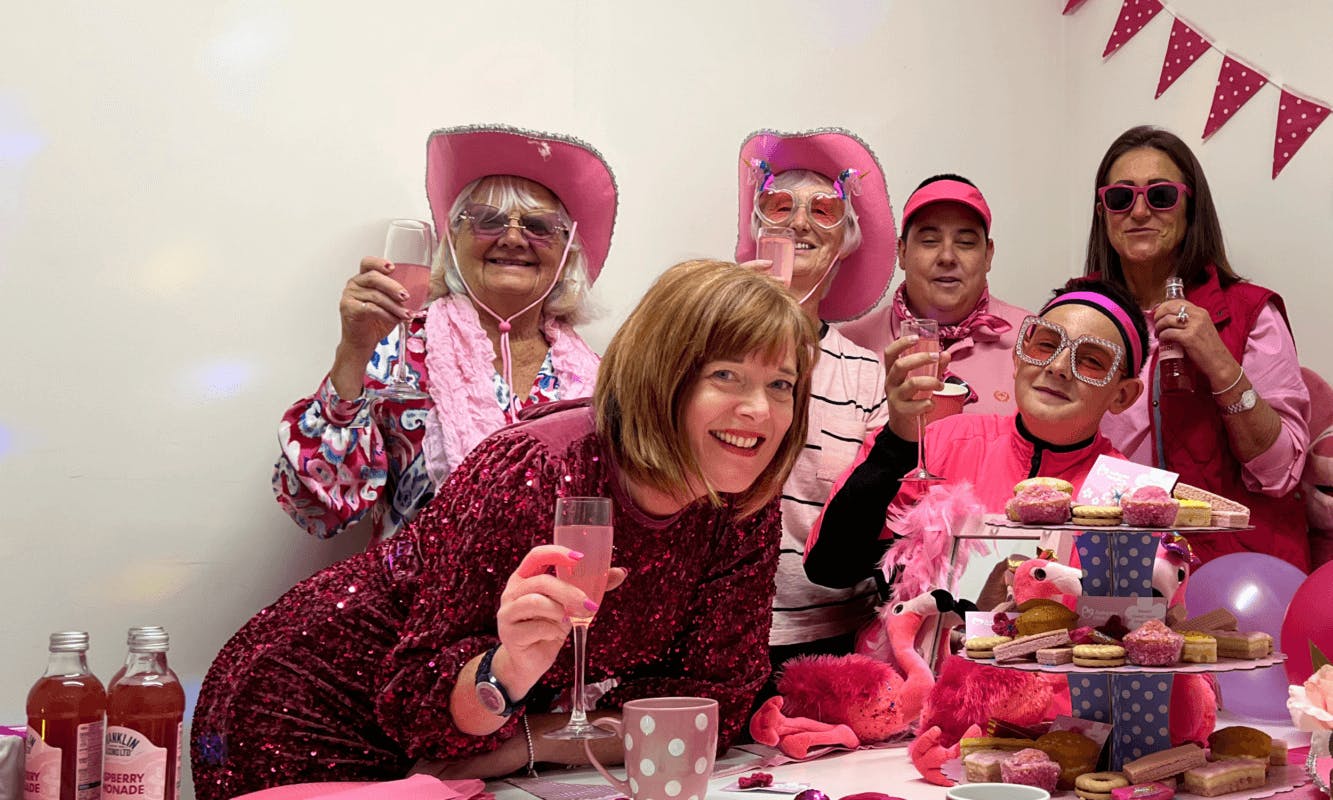 A group of people wearing flamboyant pink accessories and holding up a glass in support of an Ashgate Hospice fundraiser